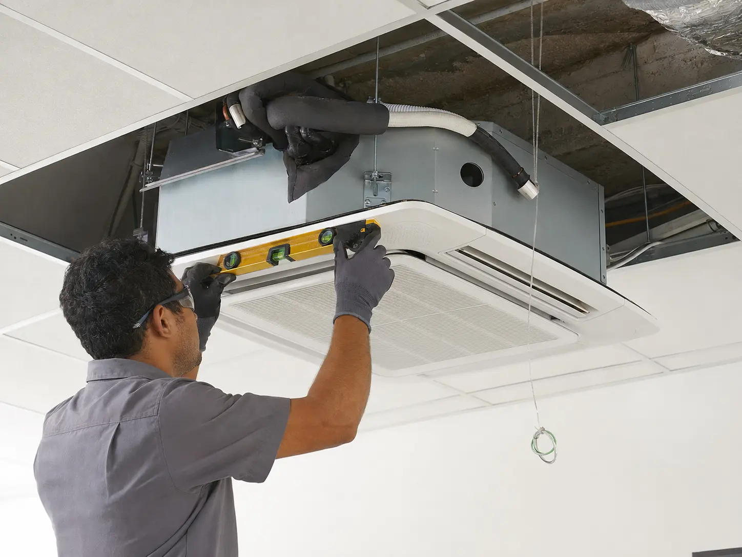 Técnico posicionando e nivelando uma unidade cassete na estrutura do teto